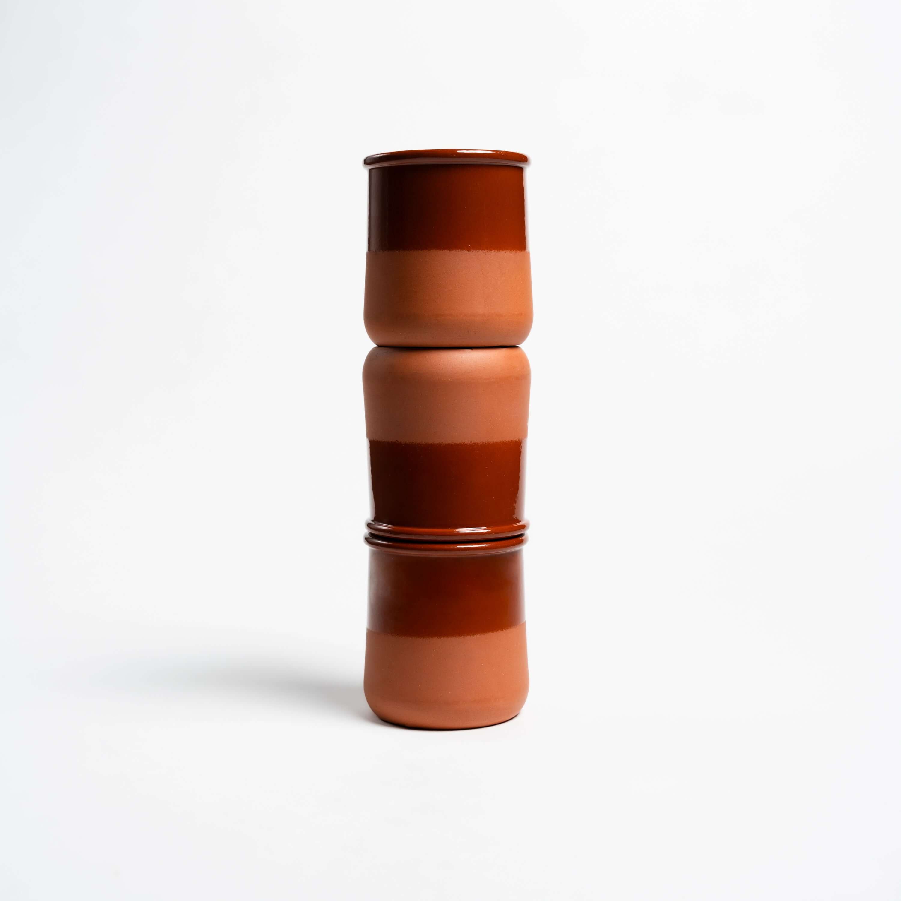 Three stacked ceramic cups with earthy brown and terracotta stripes on a white background.