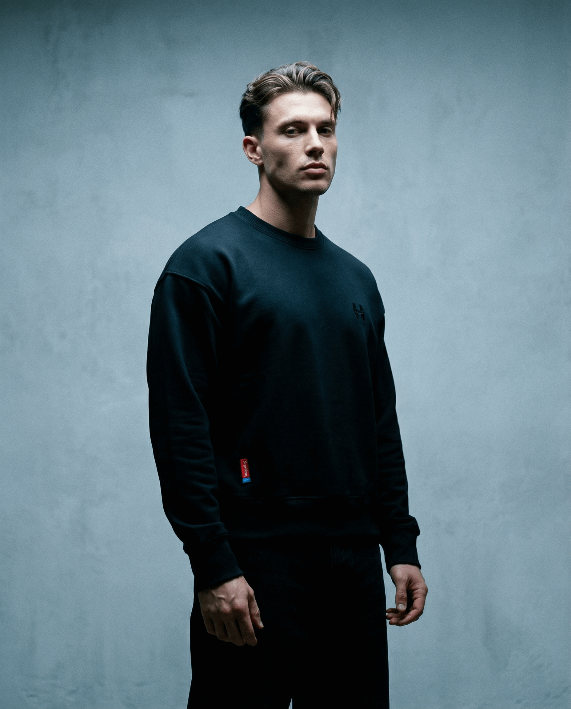 Muž v černé mikině bez kapuce s cropped oversized střihem, vyrobené z organické bavlny.