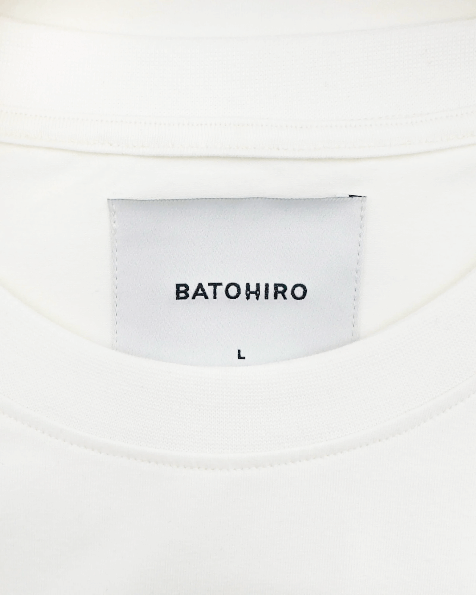 Close-up of BATOHiro label on a white cropped oversized tee, size L, showcasing quality craftsmanship.