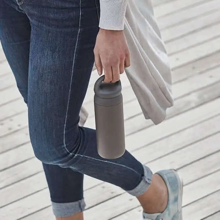 Žena drží DAY OFF Tumbler 500ml při procházce po dřevěné plošině.