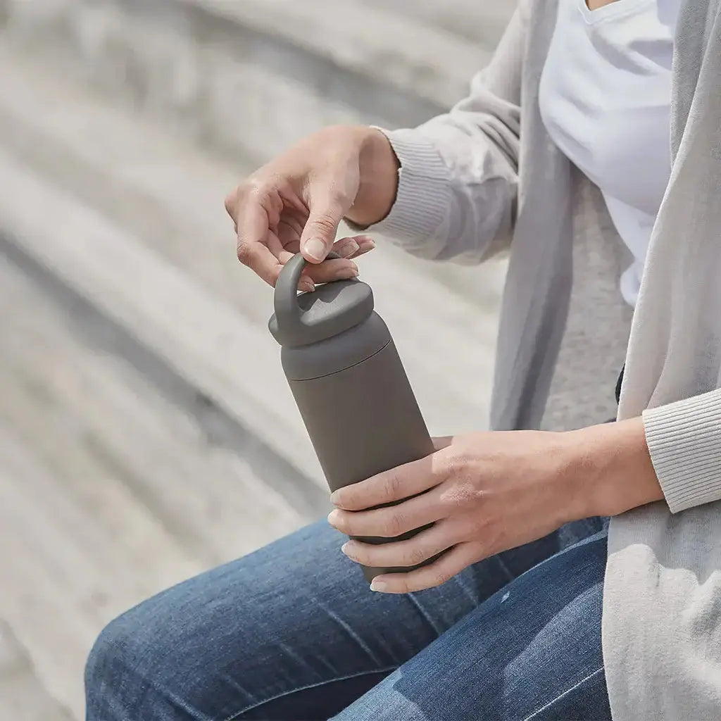 DAY OFF Tumbler 500ml being held by a person sitting on steps, showcasing its stylish design and practicality.