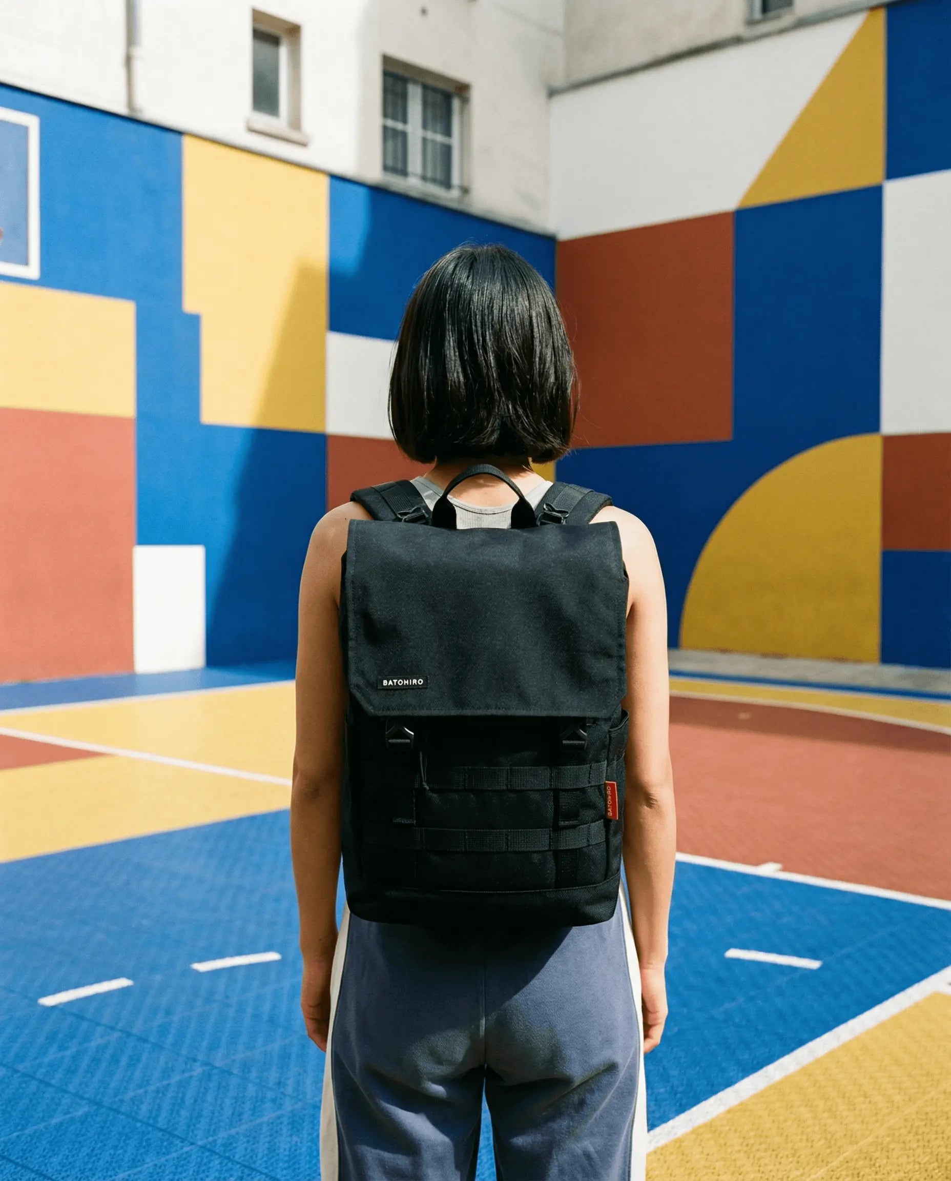Person standing with Minato Lite 2.0 - Dark Black backpack in a colorful outdoor setting.