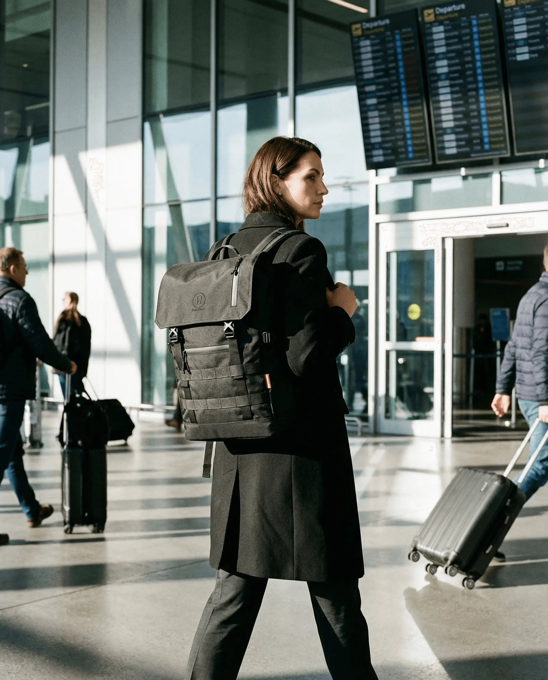 Minato Premium 6.0 – Black Knight backpack worn by a woman in an airport setting with travelers in the background.