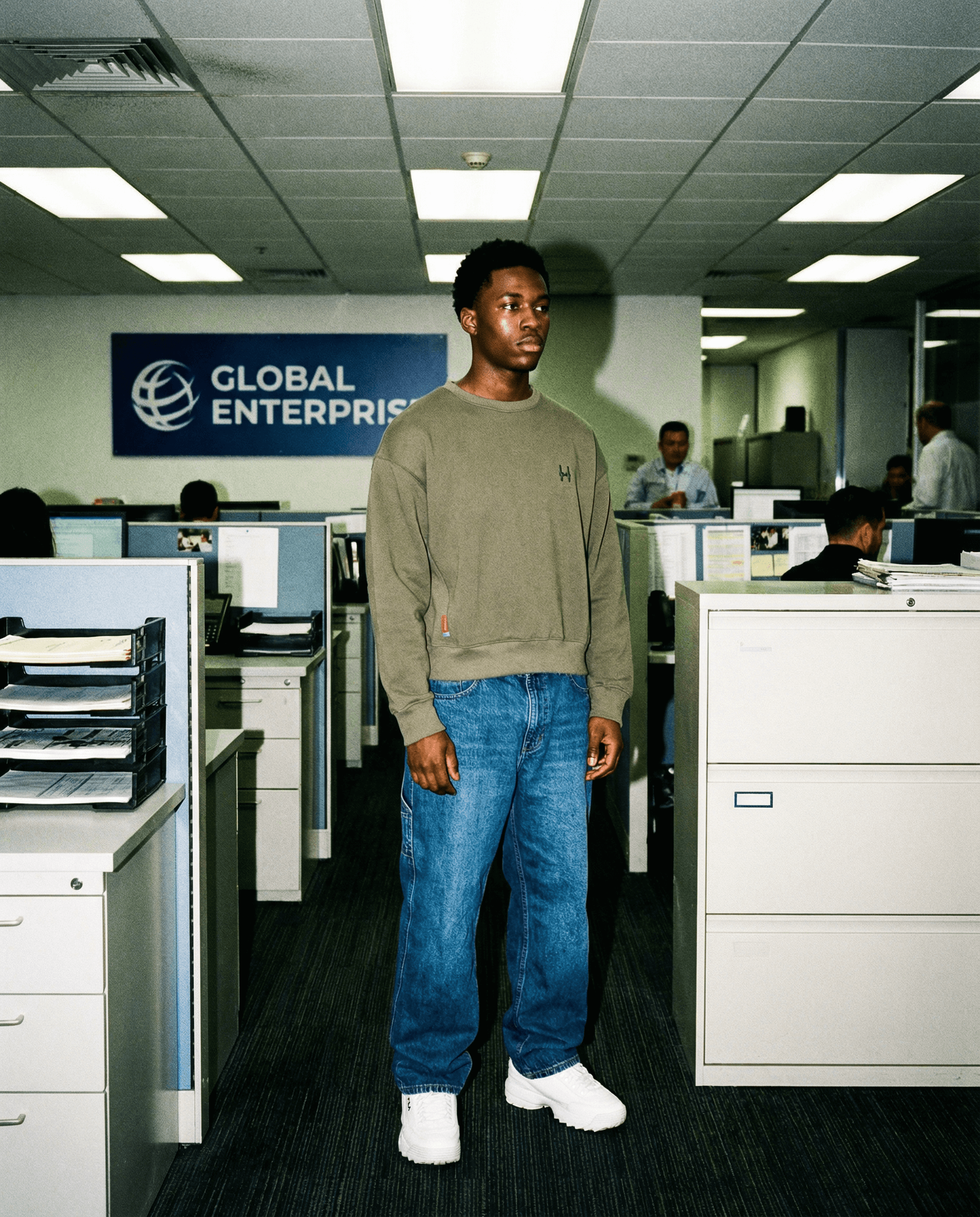 Muž v kanceláři nosící zelenou mikinu crewneck a modré džíny, s logem Global Enterprises v pozadí.